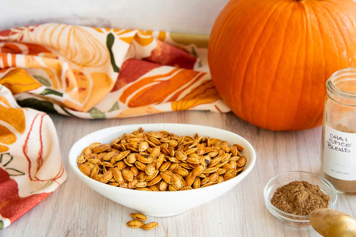 A white oval bowl filled with Chai Spiced Pumpkin Seeds.