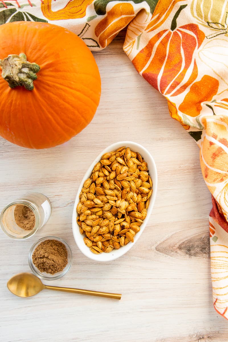 A white bowl of Chai Spiced Pumpkin Seeds next to a whole pumpkin and a bottle of Chai Spice Blend.