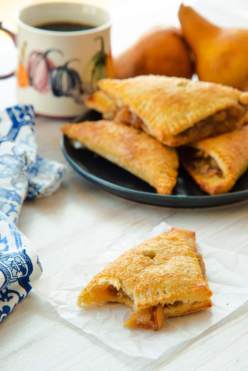 A Ginger Pear Turnover in front of a plate of turnovers and a mug of coffee.
