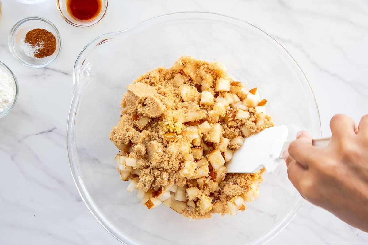 The ginger and brown sugar are stirred into the diced pears in a clear glass bowl.