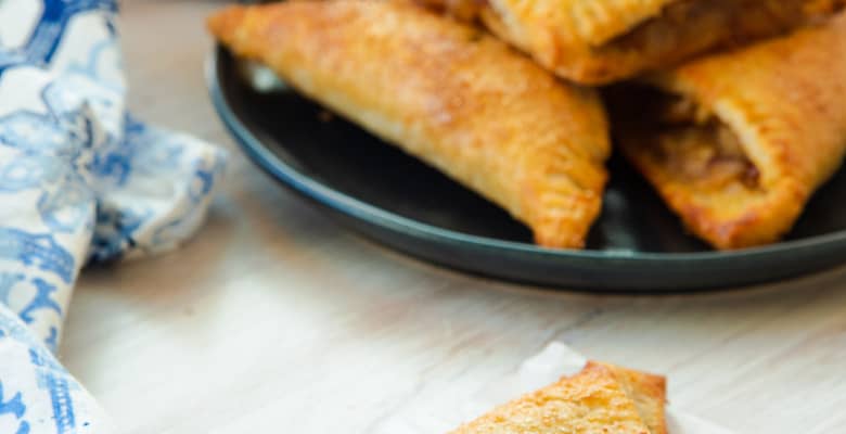 A Ginger Pear Turnover with a bite removed in front of a plate of turnovers.