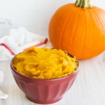 Pumpkin puree in a burgundy bowl in front of a whole pumpkin.
