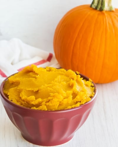 Pumpkin puree in a burgundy bowl in front of a whole pumpkin.