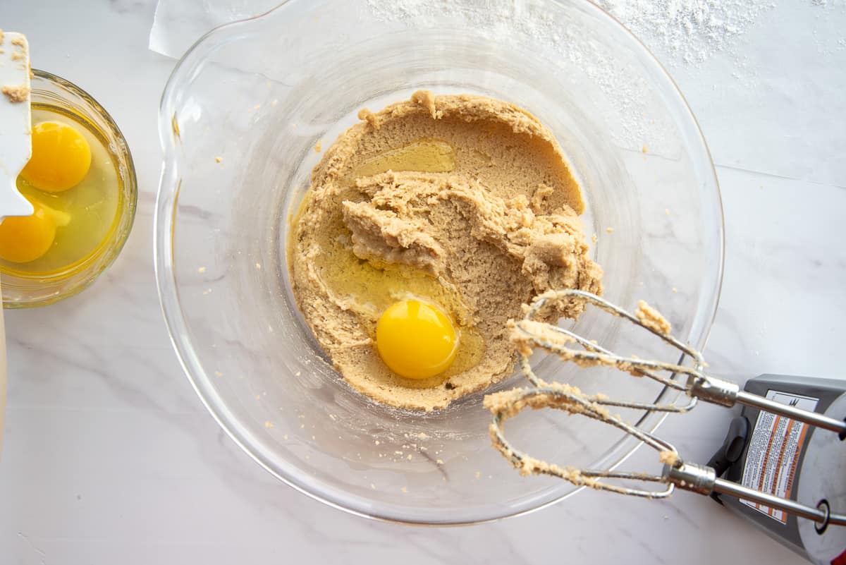 Eggs are added to the brown sugar and butter mixture in a clear glass mixing bowl.
