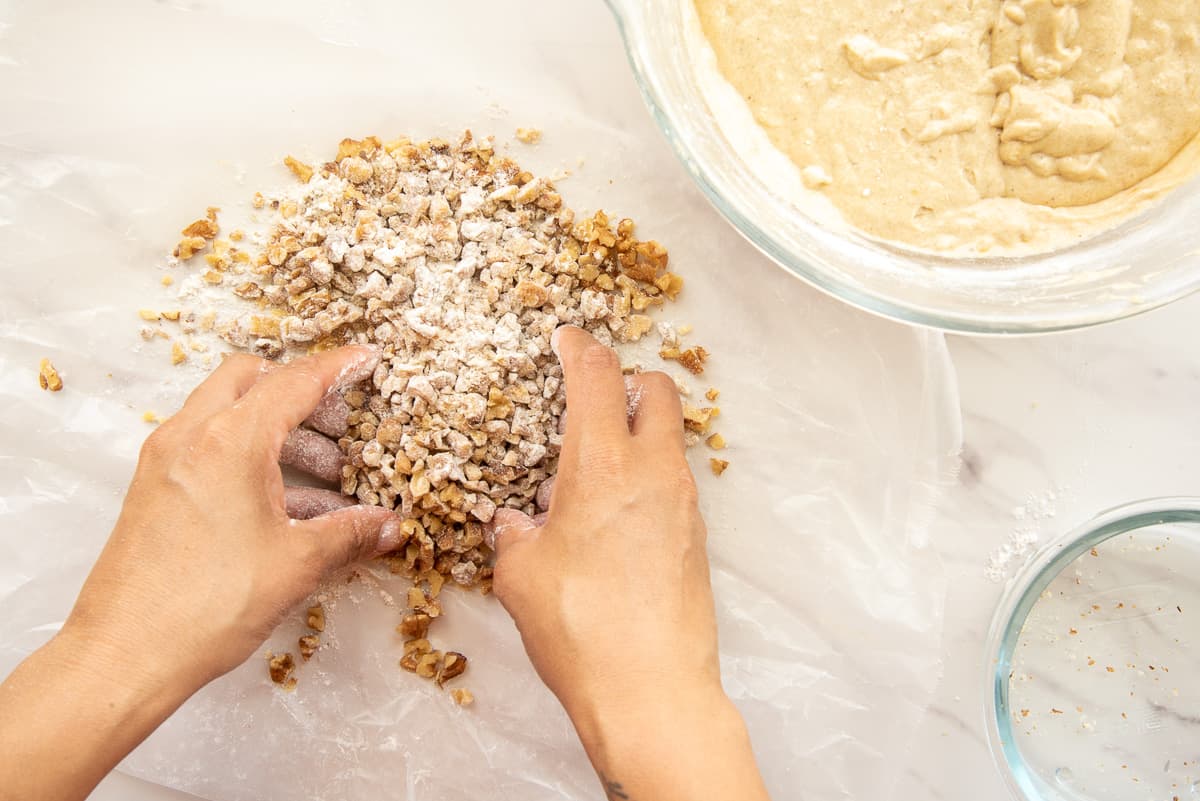 Hands toss the walnuts in flour before adding them to the batter.