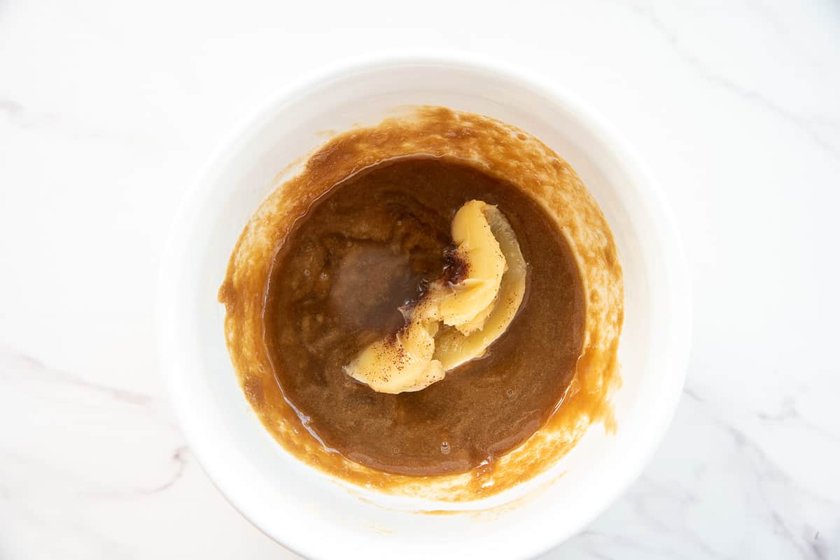 The brown butter is added to the caramel in a white mixing bowl.