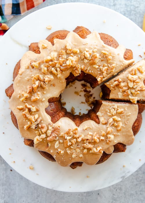 A hand uses a cake server to remove a slice of the Maple Walnut Banana Bundt Cake from the rest of the dessert.