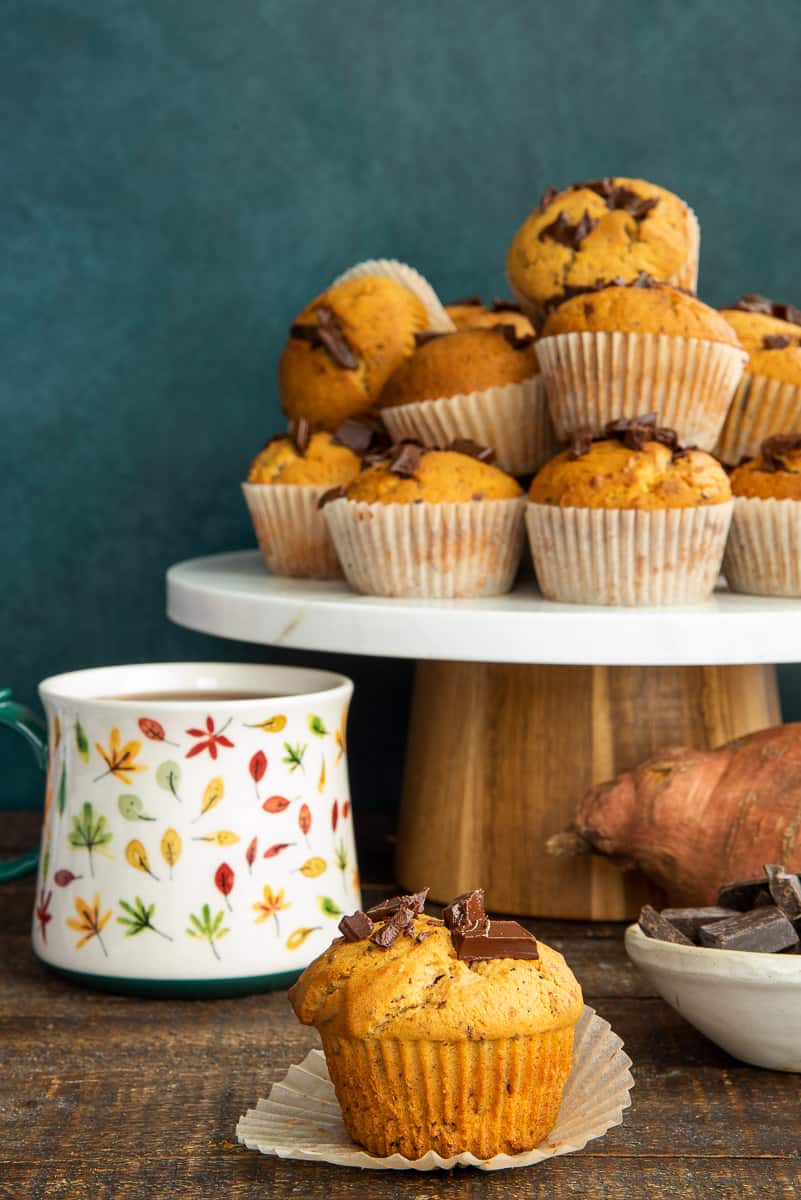 A pile of Sweet Potato Chocolate Chunk Muffins sits behind a single muffin.