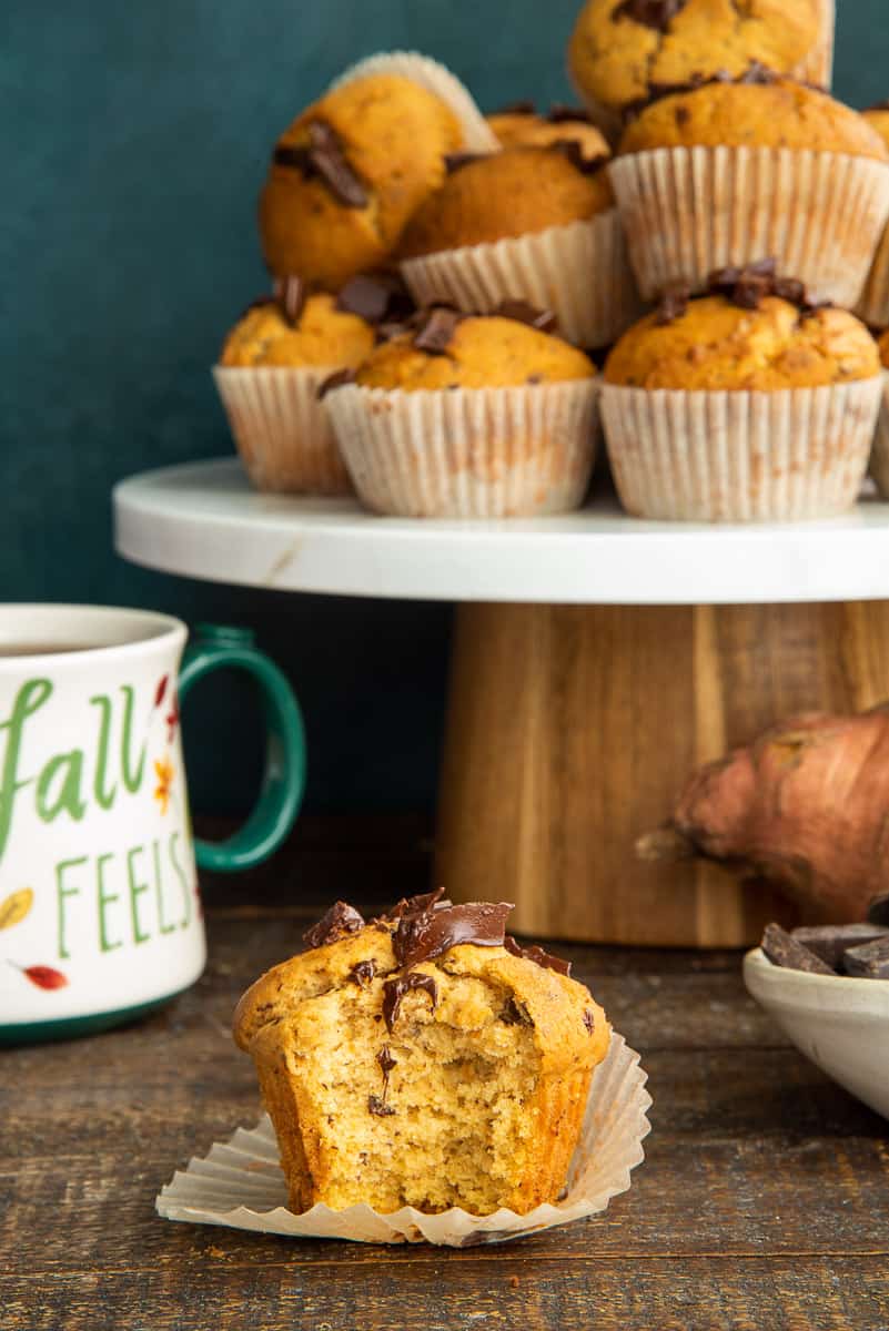 A pile of Sweet Potato Chocolate Chunk Muffins behind a single muffin with a bite removed from it.