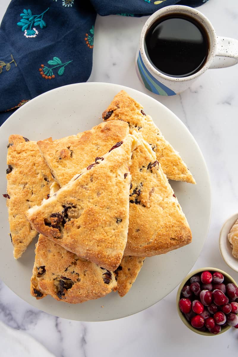 Cranberry Ginger Scones stacked on a cake plate next to a mug of tea.