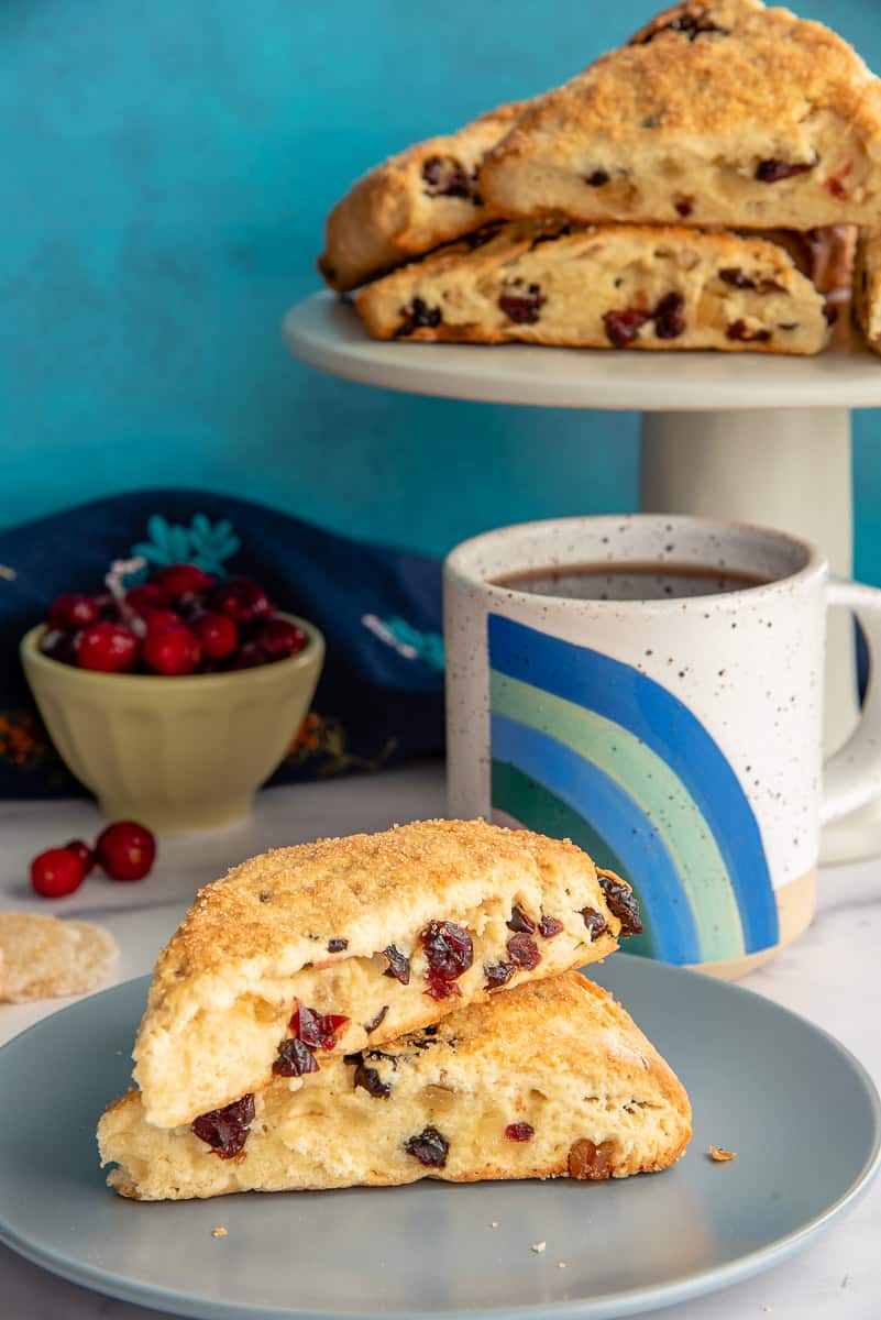 Two Cranberry Ginger Scones on a grey-blue plate next to a cake stand with the rest of the scones.