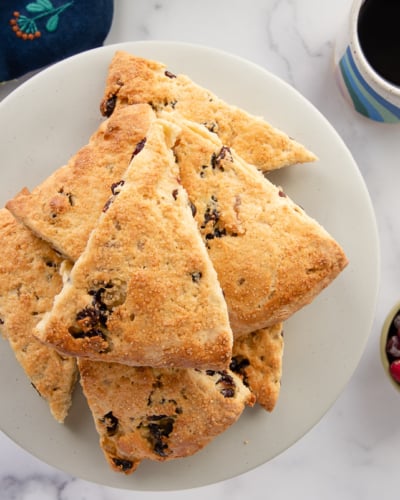 The Cranberry Ginger Scones are stacked in a pile on a marble cake stand.