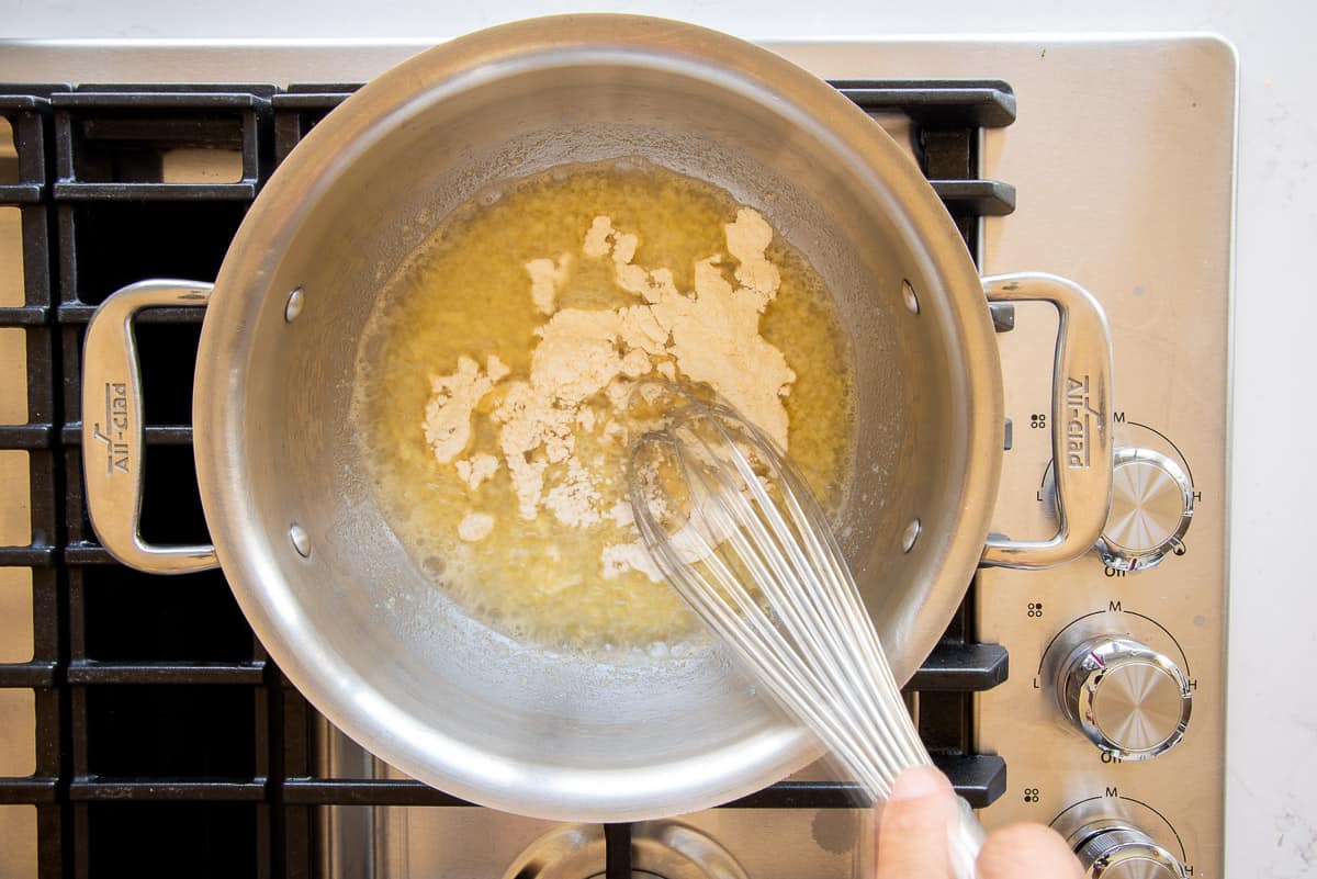 Flour is added to the brown butter in a silver pot to create a roux.