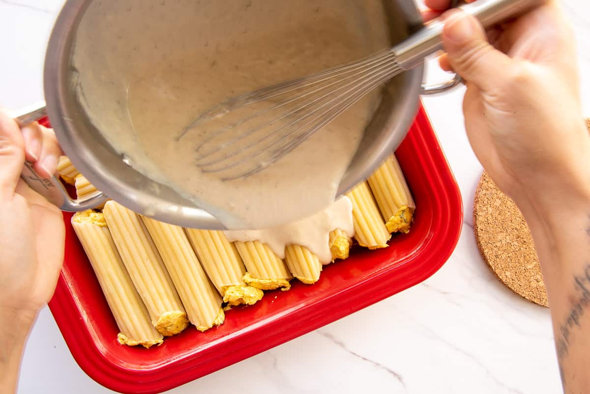 The sauce is poured over the stuffed shells in a red baking dish.