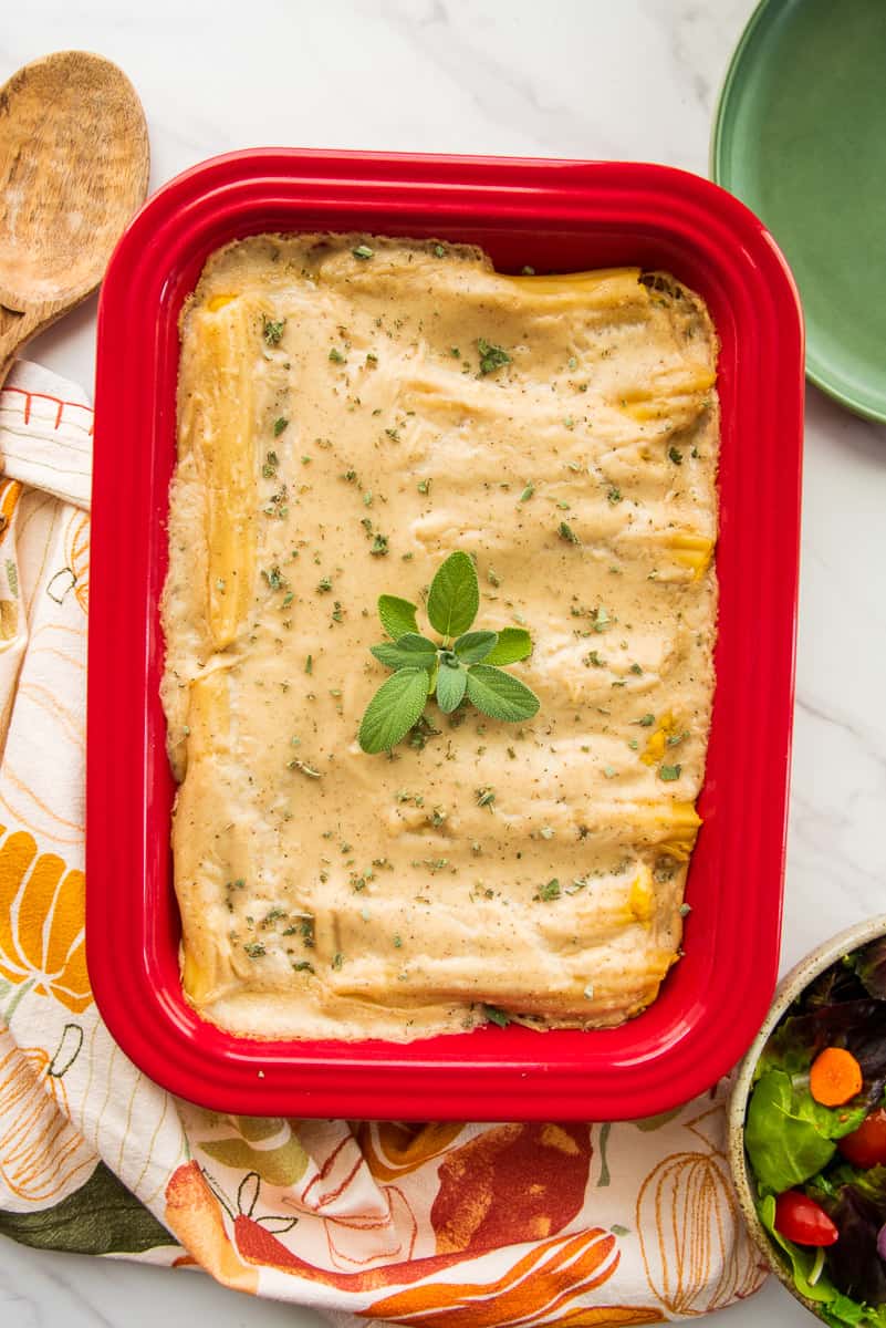 The baked Pumpkin Manicotti in Béchamel Sauce in a red baking dish garnished with fresh sage leaves.