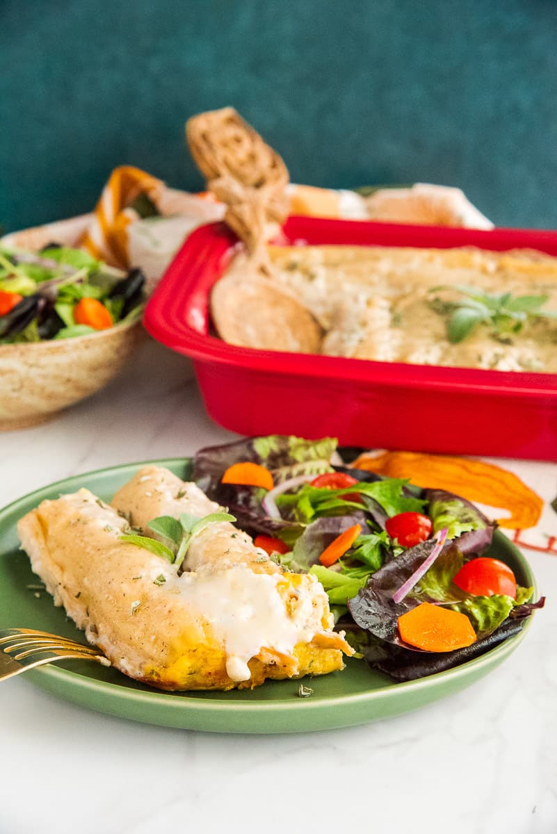 The Pumpkin Manicotti in Béchamel Sauce on a green serving plate with a side of garden salad.