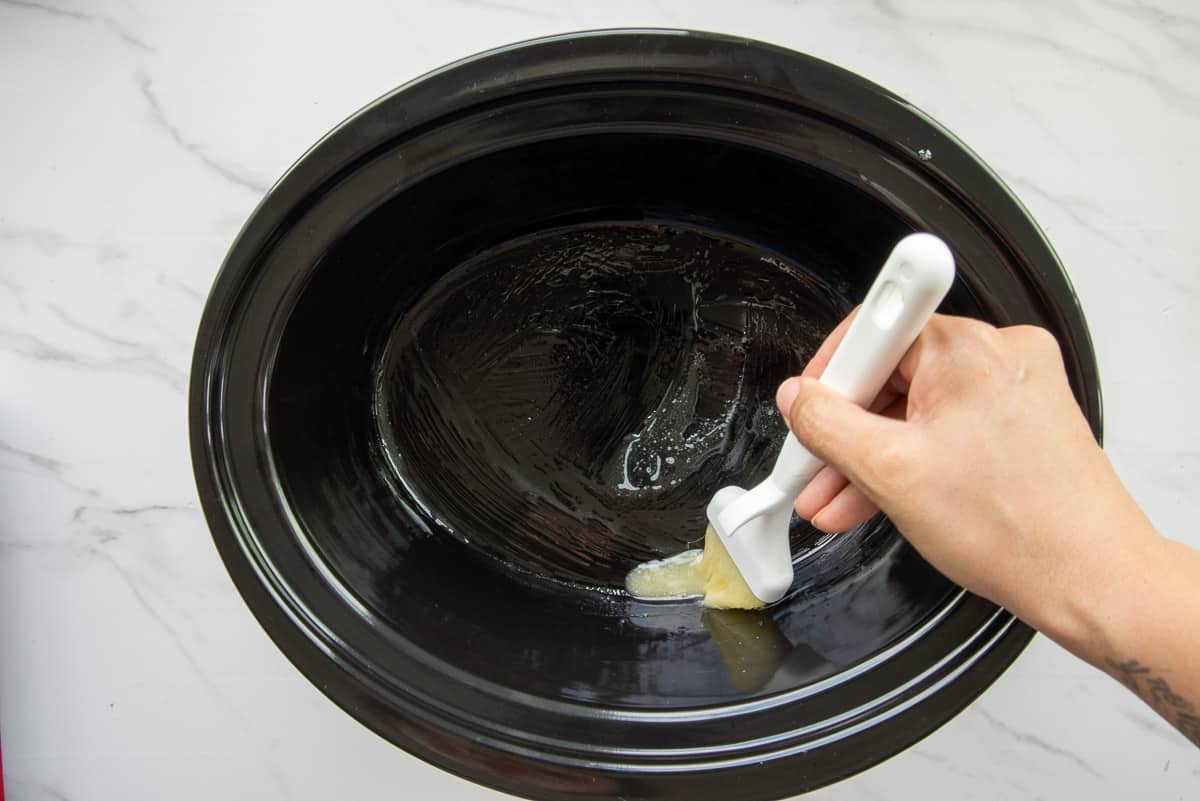 A pastry brush is used to brush some of the melted butter in the slow cooker insert.