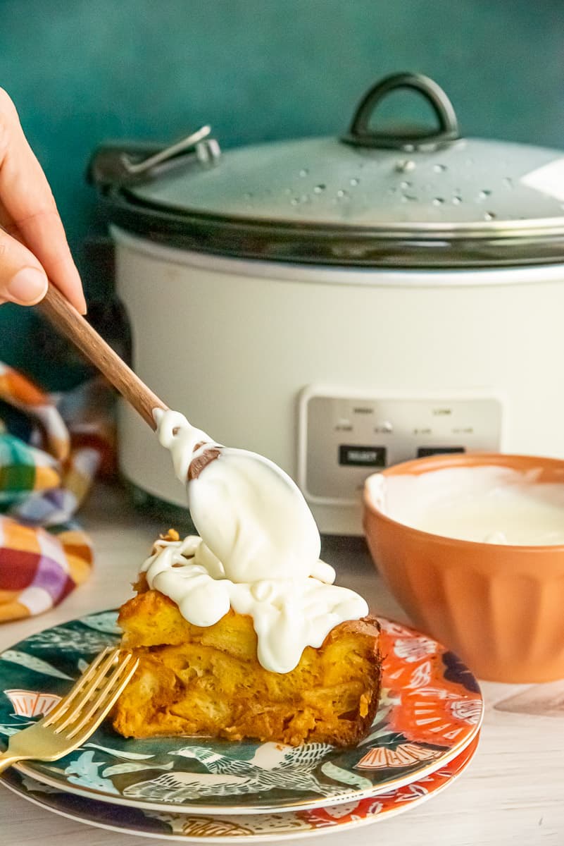 A spoons pours cream cheese glaze over a serving of Slow Cooker Pumpkin French Toast.