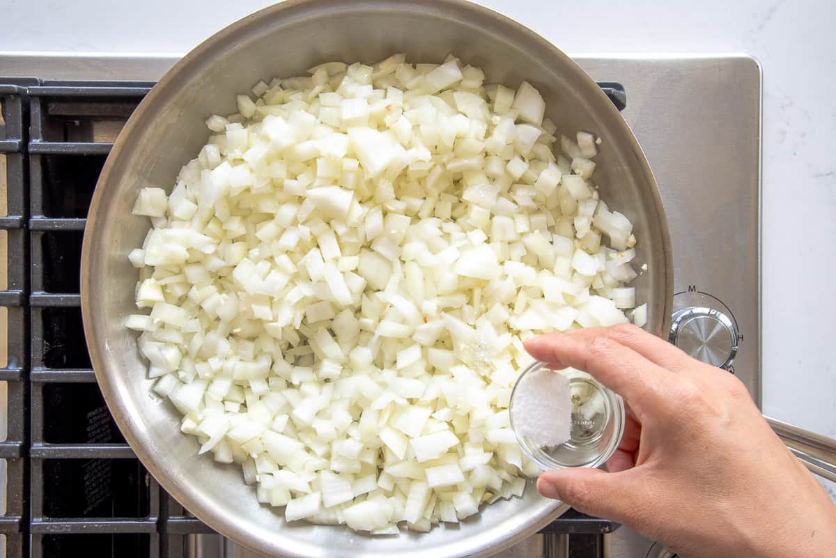 Salt is added to a sauté pan full of diced white onions.
