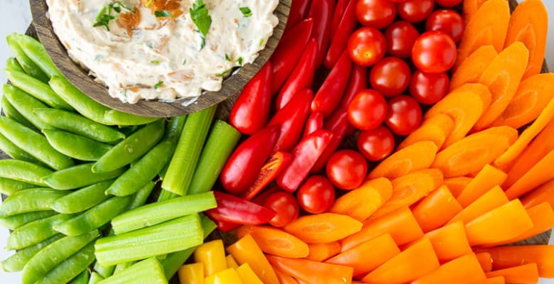 A rainbow crudité platter with a bowl of Caramelized French Onion Dip on it.