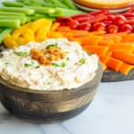 A bowl of Caramelized French Onion Dip in front of a wooden platter of crudité.