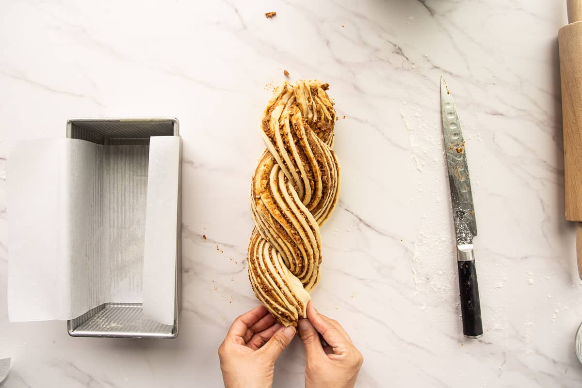 Hands twist the raw dough forming it into a two-strand braid.