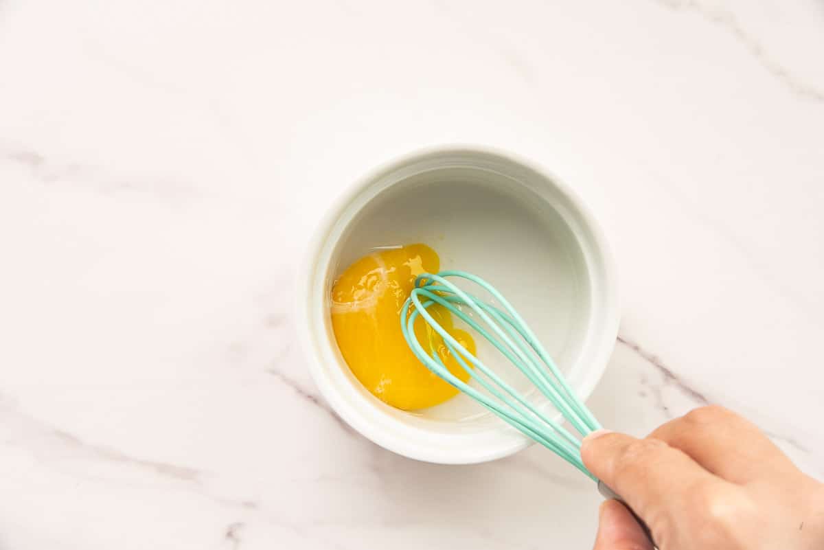 A hand uses a small whisk to combine the egg yolk and water to create an egg wash.
