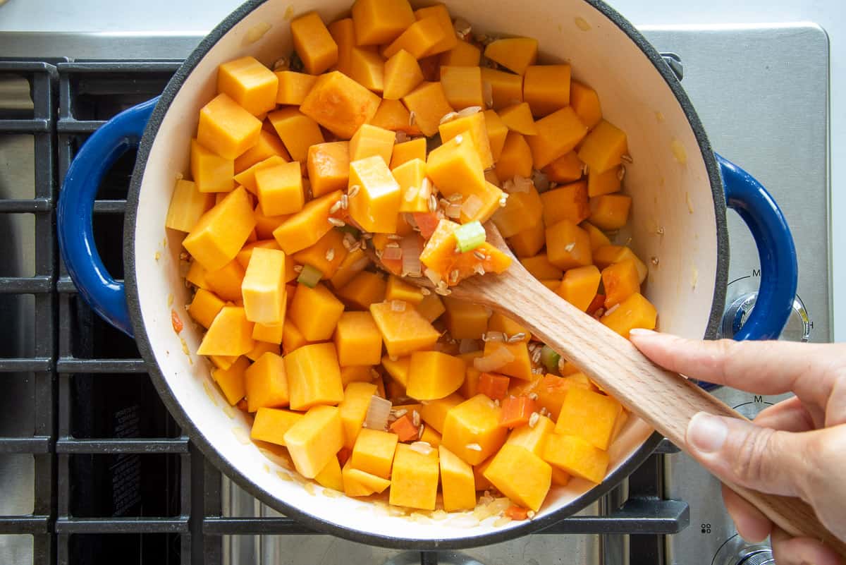 The diced butternut squash is folded into the ingredients in the dutch oven.
