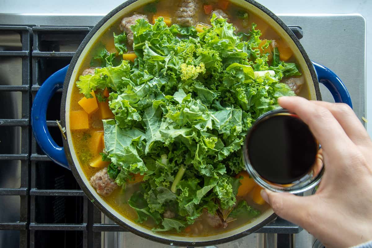 Soy sauce is added to the dutch oven with the kale.