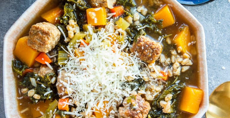 A bowl of Butternut Squash Stew with Sausage topped with shredded parmesan cheese.