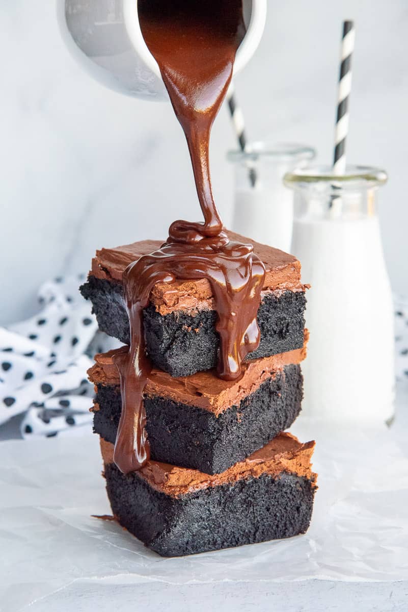 Chocolate ganache is poured over a stack of 3 dark chocolate fudgy brownies.