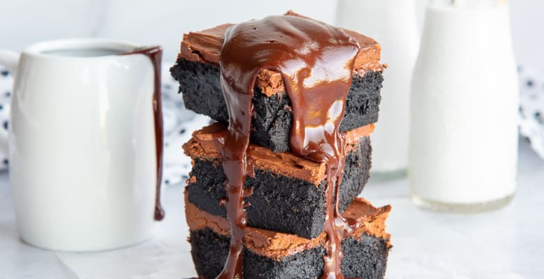 Chocolate ganache drips down the sides of a stack of three Dark Chocolate Fudgy Brownies.
