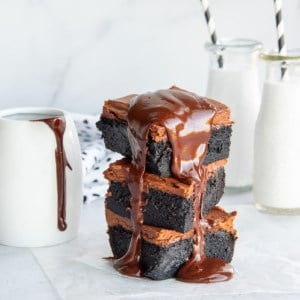 A stack of 3 dark chocolate fudgy brownies with melted ganache dripping down their sides.