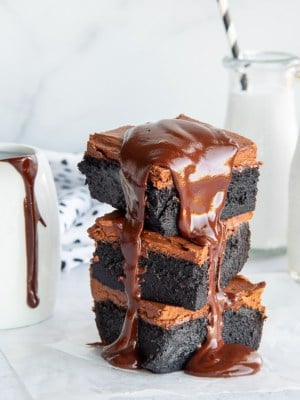 A stack of 3 dark chocolate fudgy brownies with melted ganache dripping down their sides.