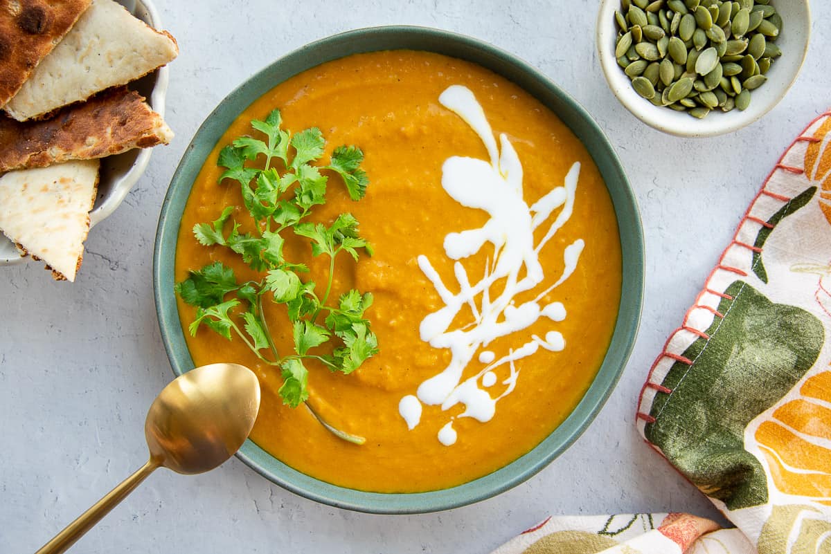 A bowl of Vegan Curry Pumpkin Soup garnished with cilantro leaves and coconut cream.