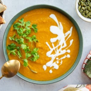 A bowl of Vegan Curry Pumpkin Soup with a gold spoon propped on it.