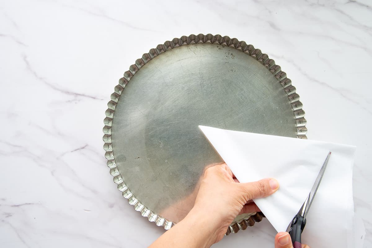 Hands hold and cut parchment to use later to line the almond tart shell before baking.