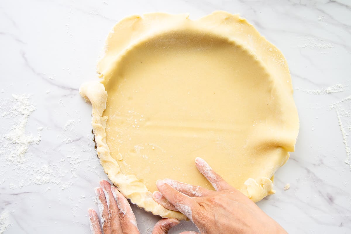 Hands for the crust on the almond tart dough inside a tart pan.