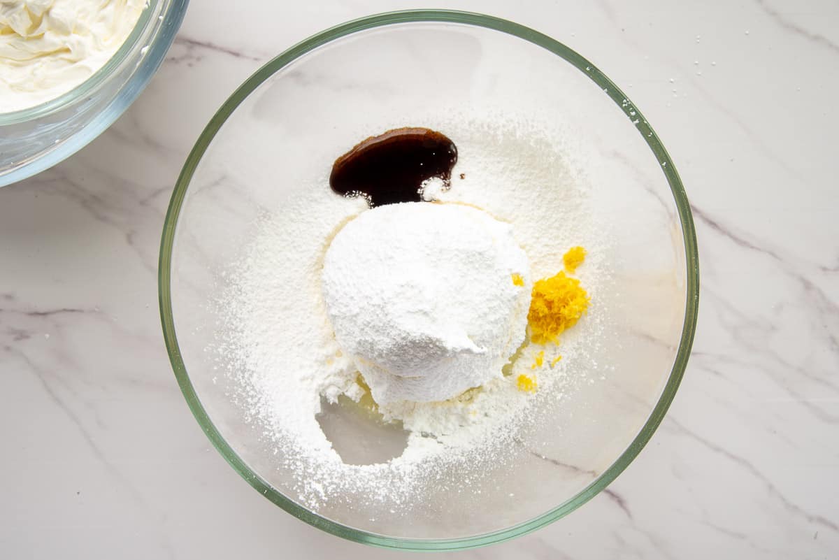 Vanilla paste, powdered sugar, lemon zest, lemon juice, and salt are added to a glass mixing bowl with mascarpone cheese.