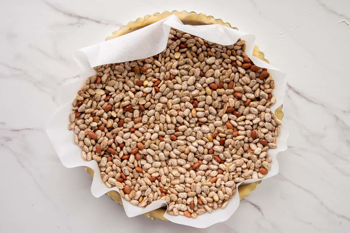 Dried beans are poured into a parchment liner inside raw tart dough before being baked.