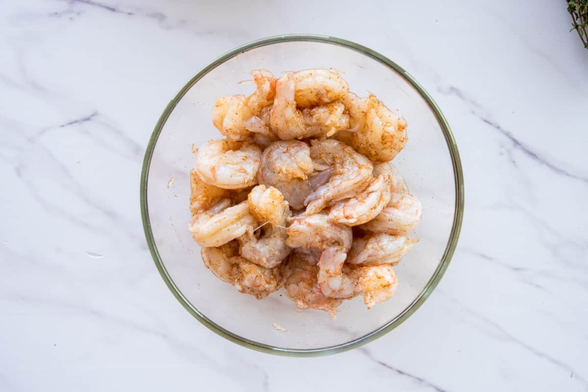 The seasoned shrimp is in a clear glass mixing bowl.