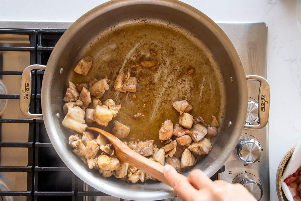 The browned chicken is removed from the pot with a slotted wooden spoon.