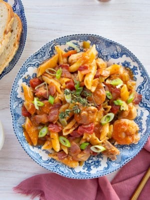 A bowlful of Jambalaya Pasta next to a loaf of sliced bread and a small bowl of sliced green onions.