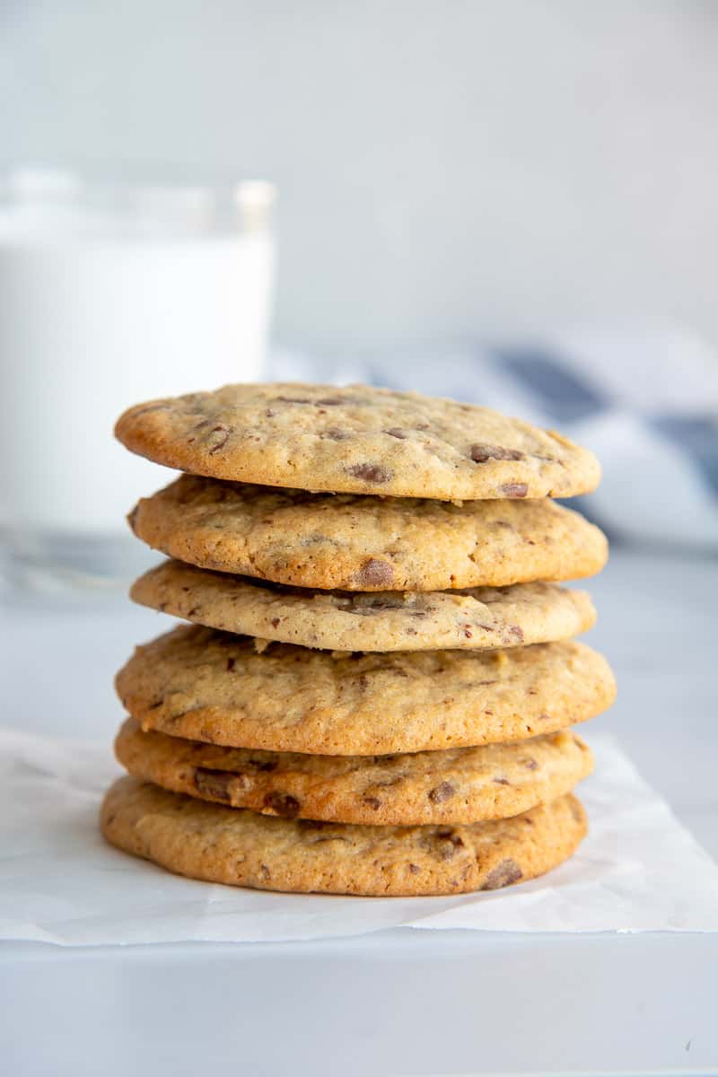 Six Rye Sourdough Discard Chocolate Chip Cookies stacked on top of one another in front of a glass of white milk.