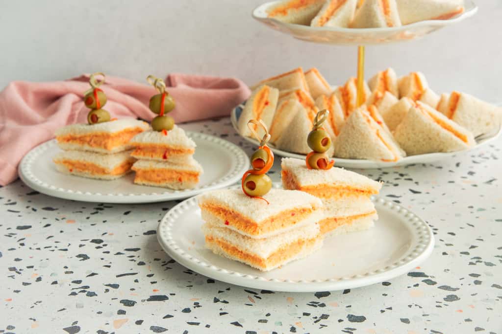 Two servings of Sandwichitos de Mezcla on white plates next to each other on a terrazzo surface.