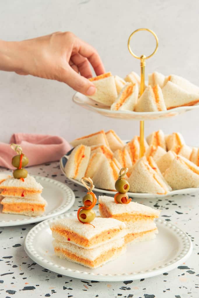 Two Sandwichitos de Mezcla on a white plate. A hand reaches for a triangle sandwich in background.