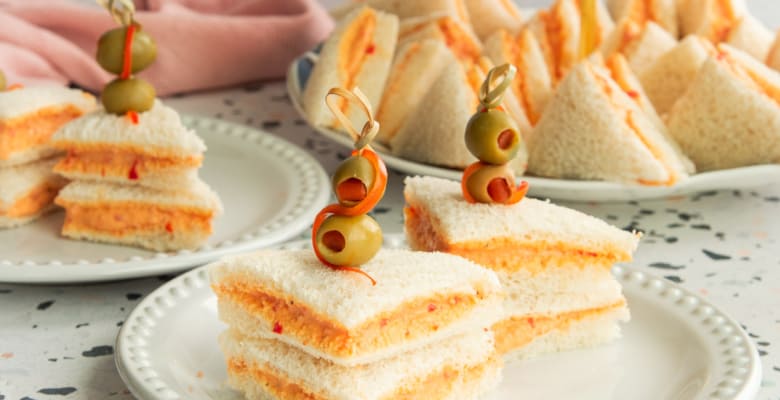 Two servings of Sandwichitos de Mezcla on a white beaded plate are garnished with olives and red pepper.