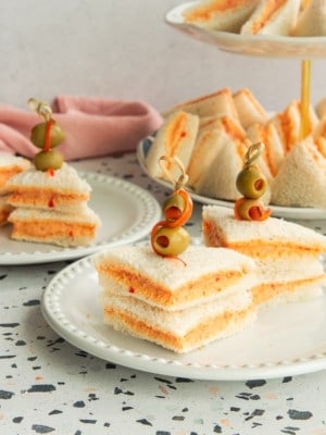 Two servings of Sandwichitos de Mezcla on white plates in front of a two-tiered serving tray.