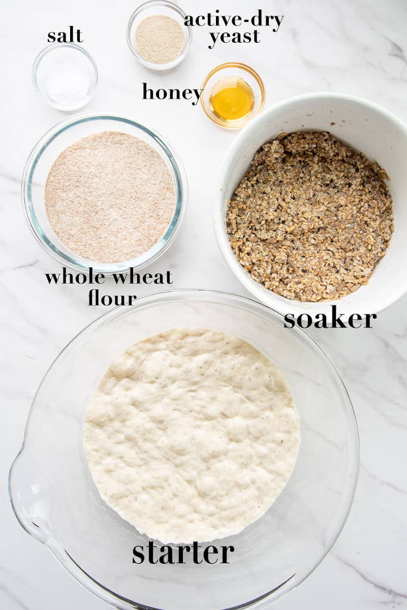 The ingredients to make Seed and Grain Sourdough Loaf are labeled and on a white countertop.