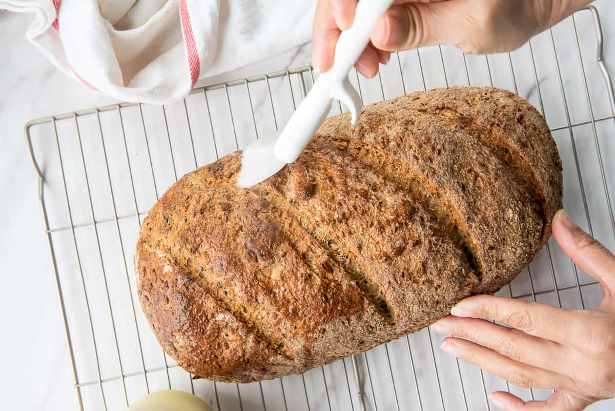One hand holds the baked bread while the other brushes water over it to give it a shiny exterior.